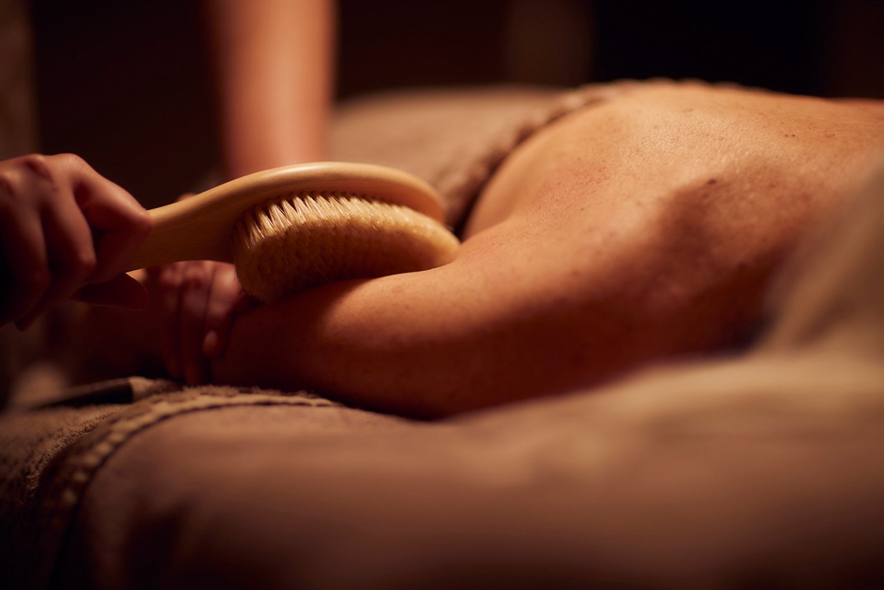 Spa therapist giving a woman a body brush treatment.