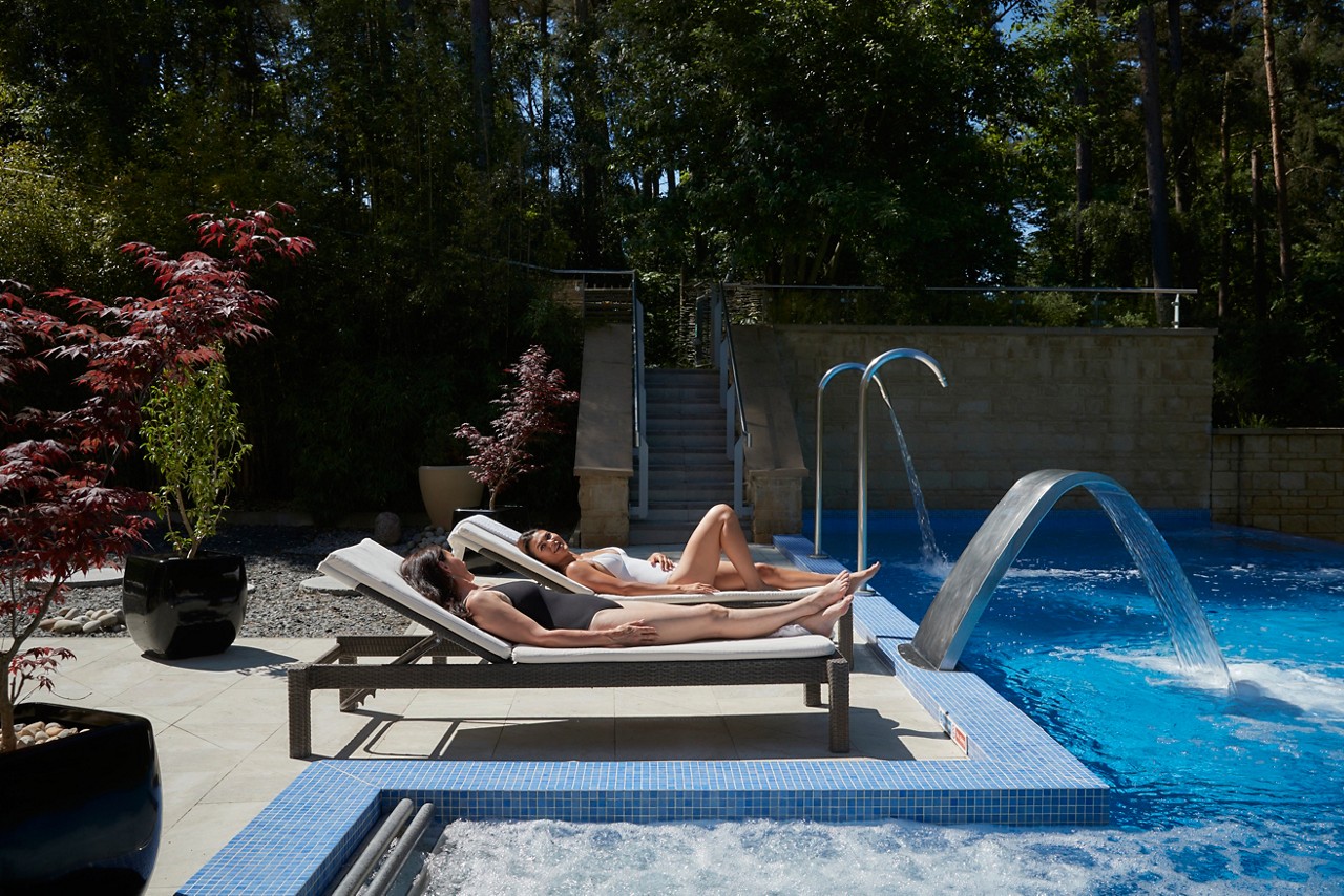 Two women relaxing on sun loungers by the pool.
