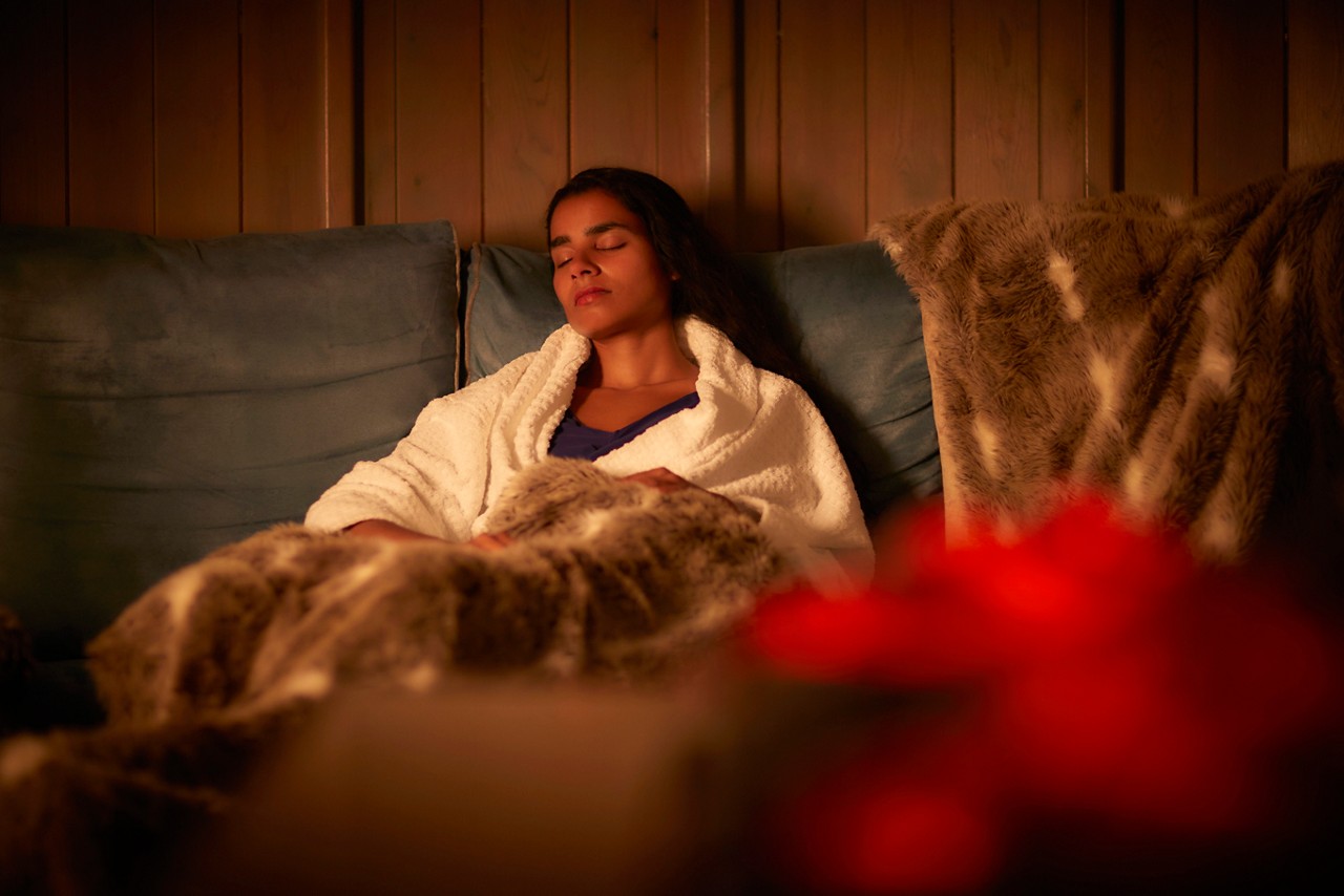 Woman snuggled under a cosy blanket beside a glowing fire.